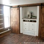 Bedroom with built-in closets and barn doors in the Platinum model P-528FPSP (Meadowview) with Chinked Log accents on display at Recreational Resort Cottages and Cabins in Rockwall, Texas.  